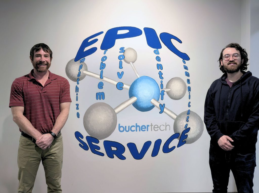 Buchertech technicians beside the EPIC IT Service wall graphic